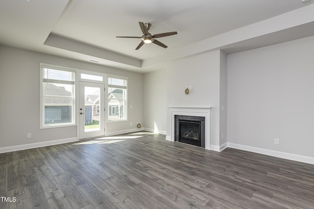 unfurnished living room with dark wood-style floors, ceiling fan, a raised ceiling, and a fireplace