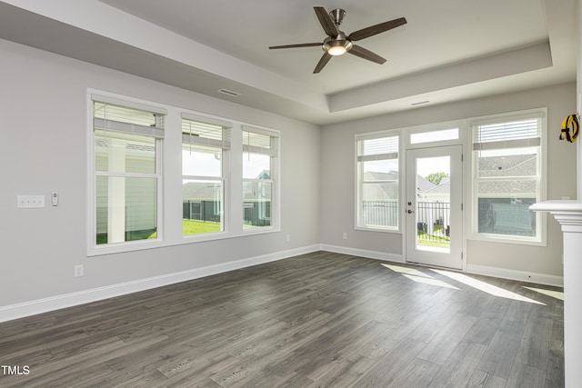 spare room with baseboards, ceiling fan, dark wood-style flooring, and a tray ceiling