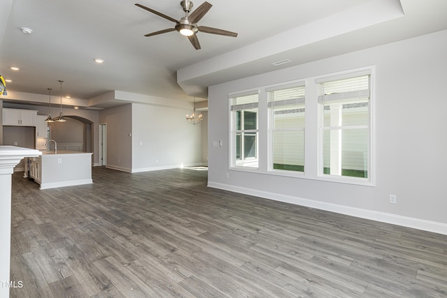 unfurnished living room featuring recessed lighting, wood finished floors, arched walkways, ceiling fan with notable chandelier, and baseboards