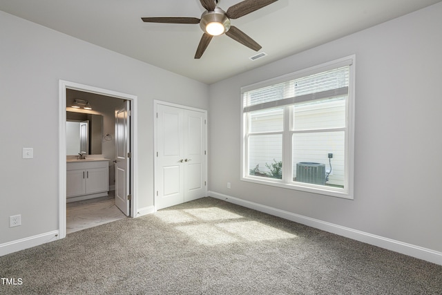 unfurnished bedroom featuring ensuite bathroom, carpet flooring, baseboards, visible vents, and a sink