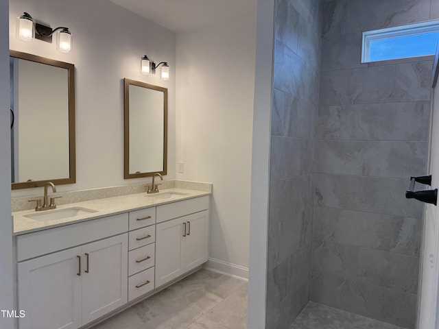 bathroom with double vanity, a sink, tiled shower, and baseboards