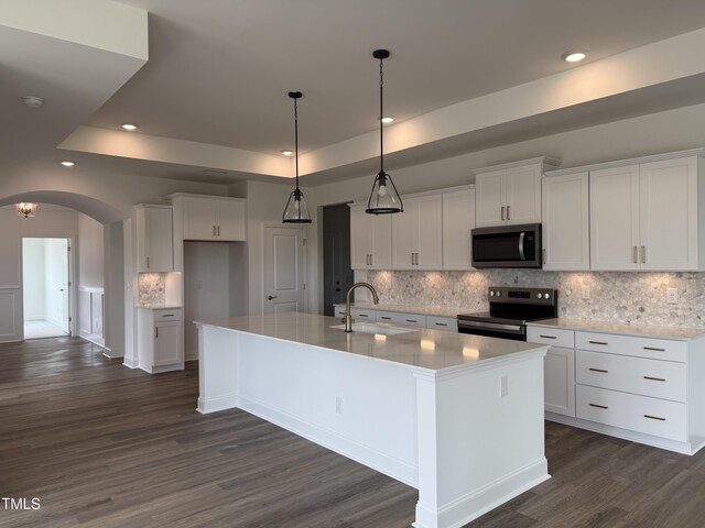 kitchen featuring arched walkways, appliances with stainless steel finishes, a raised ceiling, and a sink