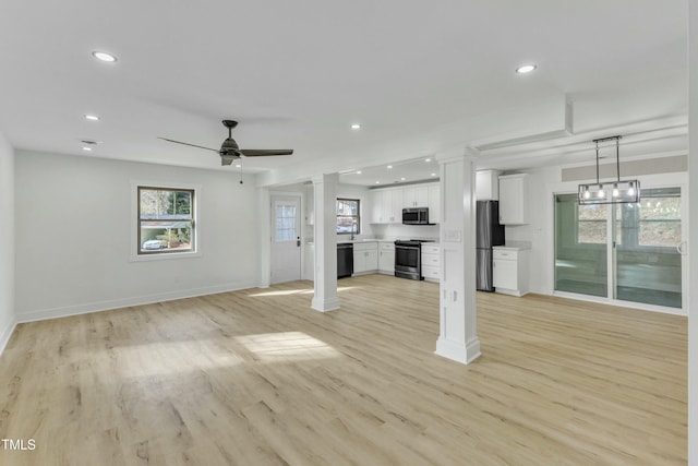 unfurnished living room featuring a wealth of natural light, decorative columns, ceiling fan, and light wood-type flooring