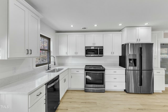 kitchen featuring sink, light stone counters, appliances with stainless steel finishes, light hardwood / wood-style floors, and white cabinets