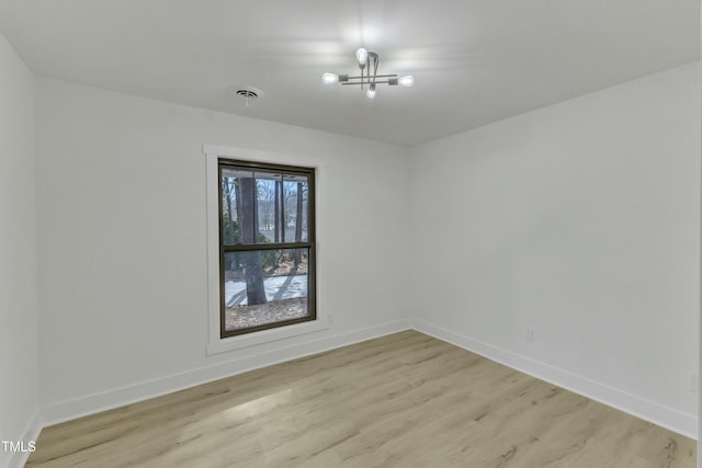 unfurnished room with a notable chandelier and light wood-type flooring