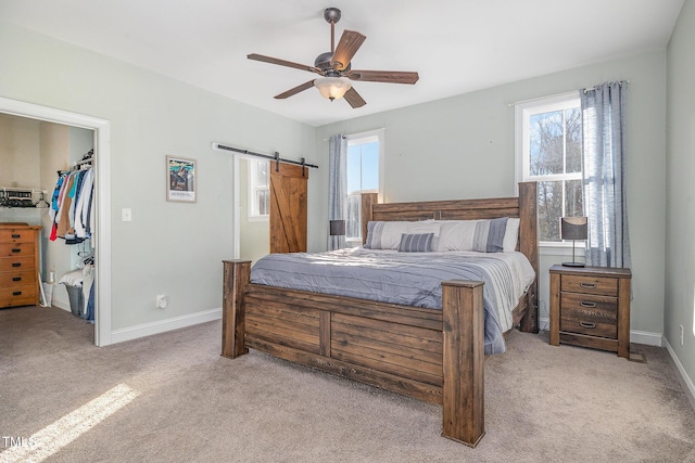 bedroom with multiple windows, a walk in closet, light colored carpet, and a barn door