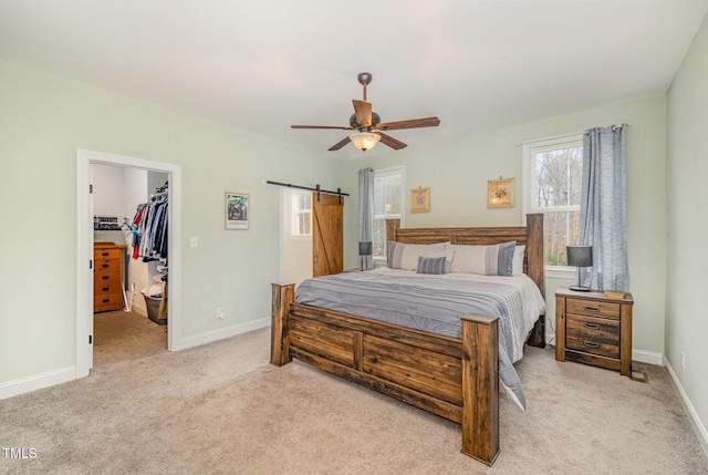 bedroom with ceiling fan, a barn door, a spacious closet, light colored carpet, and a closet