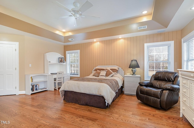 bedroom featuring ceiling fan, a raised ceiling, and light wood-type flooring