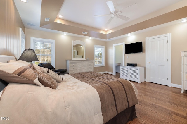 bedroom with multiple windows, wood-type flooring, a raised ceiling, and ceiling fan