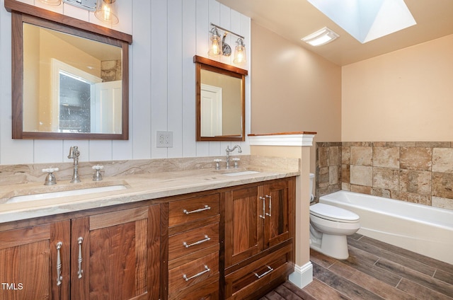 bathroom featuring toilet, a skylight, vanity, hardwood / wood-style floors, and a washtub