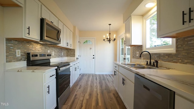 kitchen with sink, white cabinetry, hanging light fixtures, appliances with stainless steel finishes, and hardwood / wood-style floors