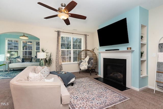 carpeted living room with built in shelves and ceiling fan