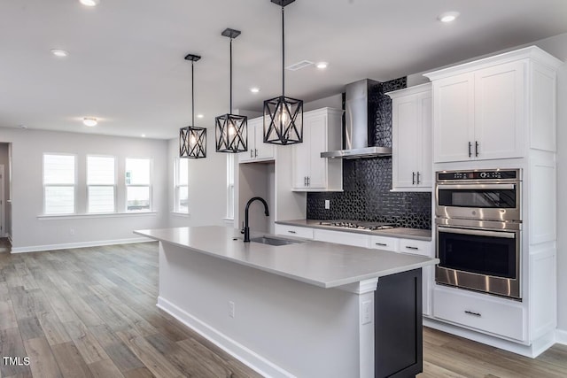 kitchen featuring sink, decorative light fixtures, wall chimney range hood, and an island with sink