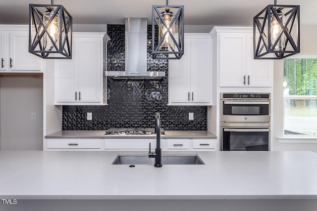 kitchen with wall chimney exhaust hood, stainless steel appliances, sink, and hanging light fixtures