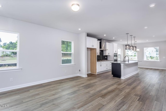 kitchen featuring hardwood / wood-style floors, white cabinets, hanging light fixtures, a center island with sink, and wall chimney exhaust hood