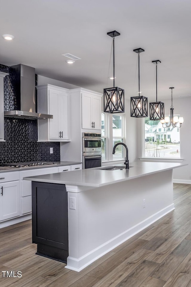 kitchen with a center island with sink, sink, wall chimney range hood, and white cabinets