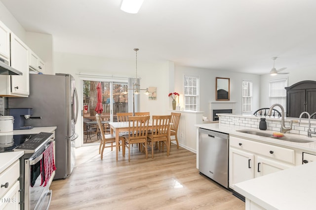 kitchen with sink, white cabinetry, light wood-type flooring, appliances with stainless steel finishes, and pendant lighting