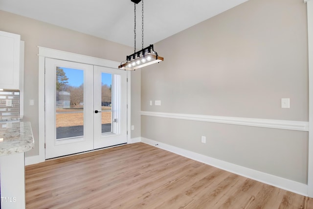 unfurnished dining area featuring french doors and light hardwood / wood-style flooring