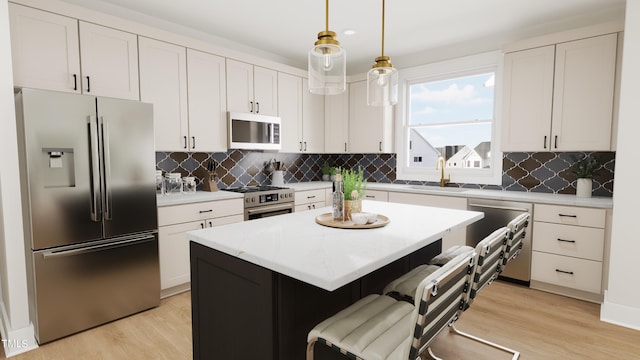 kitchen with white cabinetry, hanging light fixtures, light hardwood / wood-style flooring, appliances with stainless steel finishes, and a kitchen island