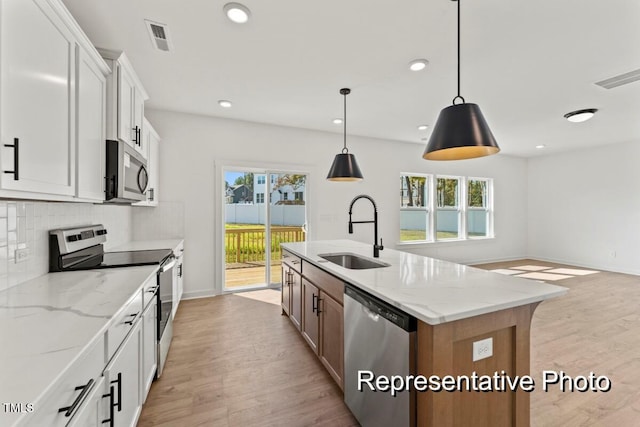 kitchen with decorative light fixtures, an island with sink, sink, white cabinets, and stainless steel appliances