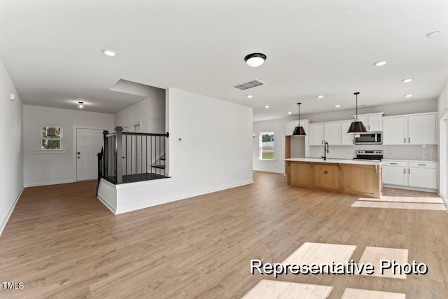 kitchen with pendant lighting, white cabinetry, stainless steel appliances, light wood-type flooring, and a spacious island