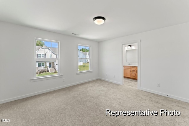 unfurnished bedroom with ensuite bath and light colored carpet