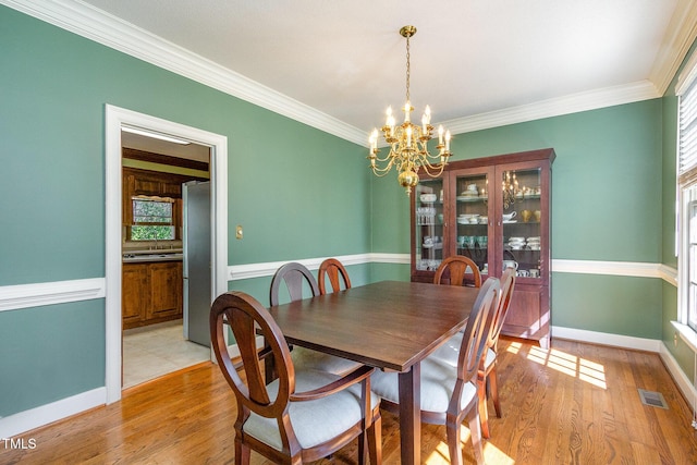 dining room with visible vents, ornamental molding, light wood-style flooring, baseboards, and a chandelier