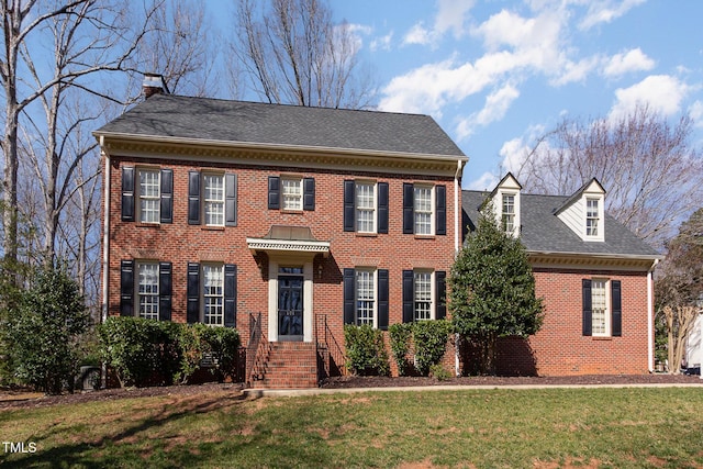 colonial inspired home with brick siding, a chimney, and a front yard