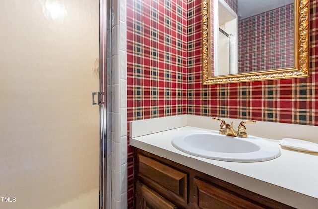 full bathroom with a stall shower, vanity, and wallpapered walls