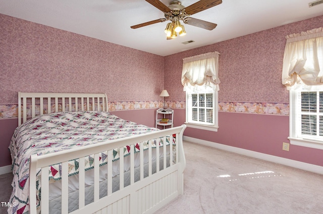 carpeted bedroom featuring wallpapered walls, visible vents, baseboards, and ceiling fan