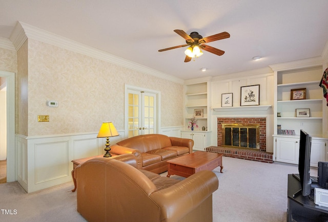 living area featuring a ceiling fan, wainscoting, wallpapered walls, crown molding, and light colored carpet