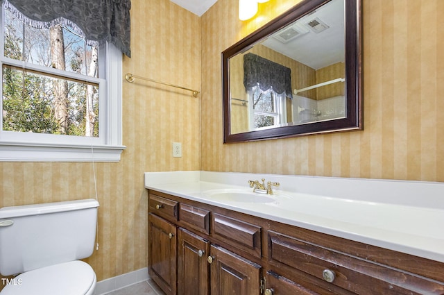 bathroom featuring toilet, wallpapered walls, vanity, and baseboards