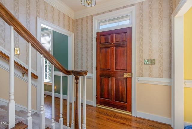 foyer featuring stairway, wood finished floors, baseboards, wallpapered walls, and ornamental molding