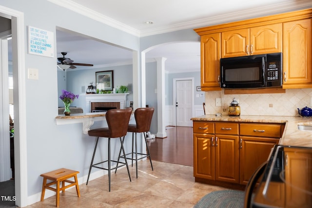 kitchen with crown molding, stove, tasteful backsplash, light stone countertops, and a brick fireplace