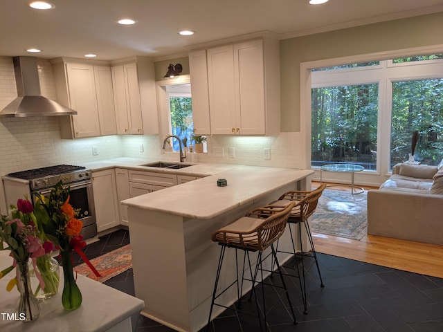 kitchen with white cabinetry, sink, a breakfast bar area, gas range, and wall chimney range hood