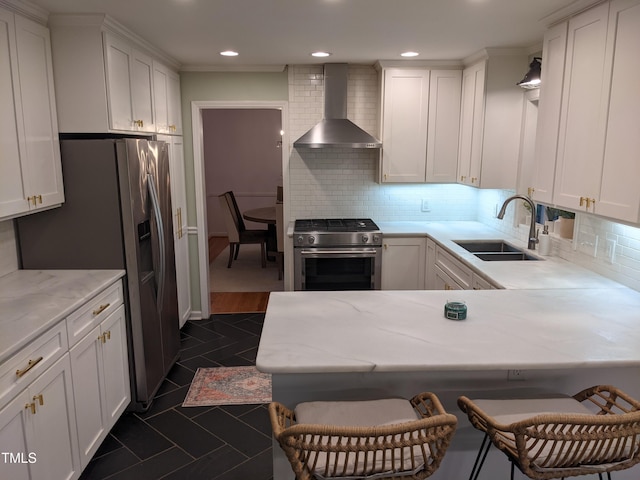 kitchen with wall chimney range hood, a breakfast bar, white cabinets, and appliances with stainless steel finishes