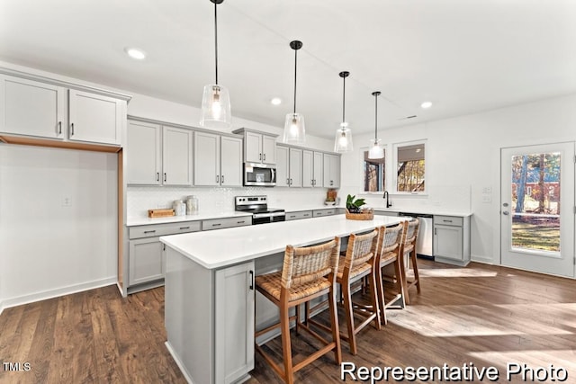 kitchen featuring a breakfast bar area, gray cabinetry, hanging light fixtures, stainless steel appliances, and a kitchen island