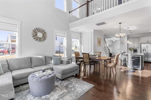 living room with wine cooler, dark wood-type flooring, sink, a chandelier, and a towering ceiling