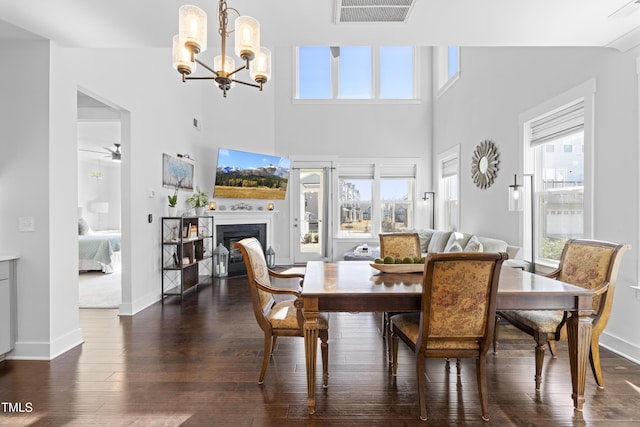 dining area featuring a healthy amount of sunlight, dark hardwood / wood-style floors, ceiling fan with notable chandelier, and a high ceiling