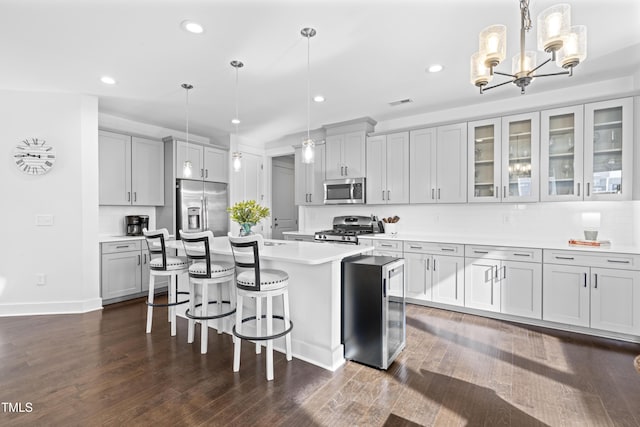 kitchen with hanging light fixtures, appliances with stainless steel finishes, a kitchen island with sink, and a kitchen bar