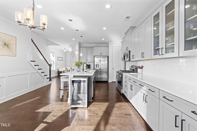 kitchen with a kitchen island with sink, decorative light fixtures, stainless steel appliances, and beverage cooler