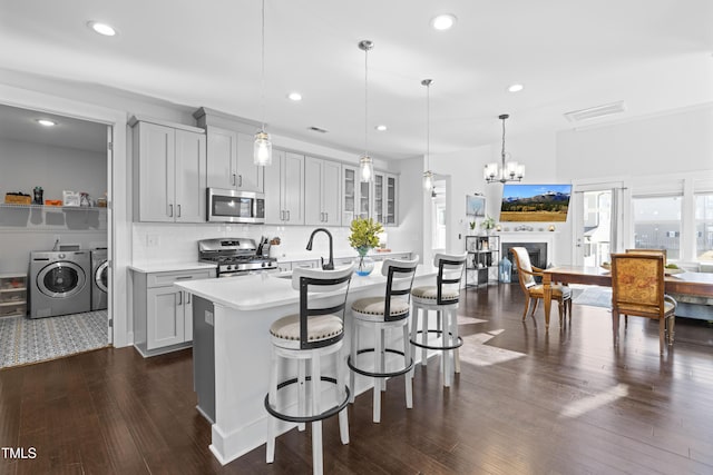 kitchen with sink, appliances with stainless steel finishes, hanging light fixtures, washing machine and clothes dryer, and a center island with sink