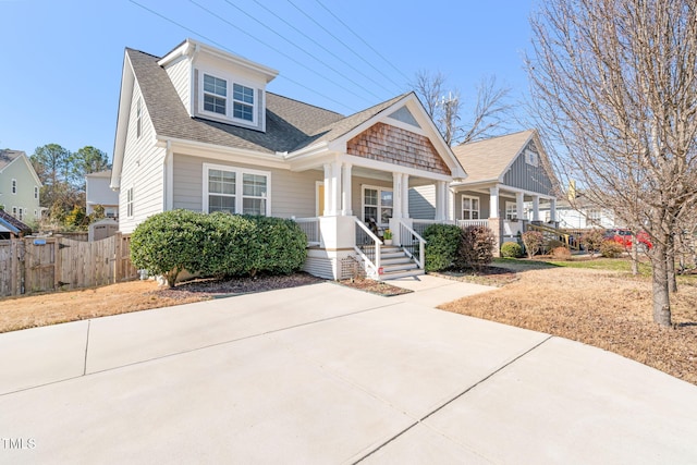 view of front of property featuring a shingled roof, covered porch, and fence