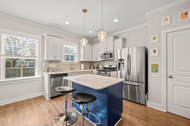 kitchen featuring hanging light fixtures, appliances with stainless steel finishes, white cabinets, a kitchen island, and a sink