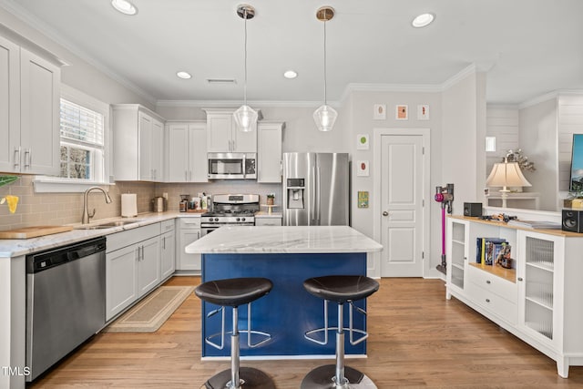 kitchen with appliances with stainless steel finishes, white cabinets, a sink, and a kitchen island