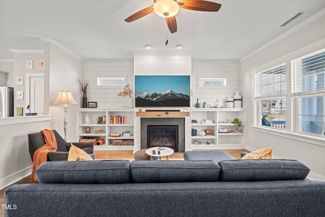 living room with wood finished floors, ornamental molding, a glass covered fireplace, and visible vents