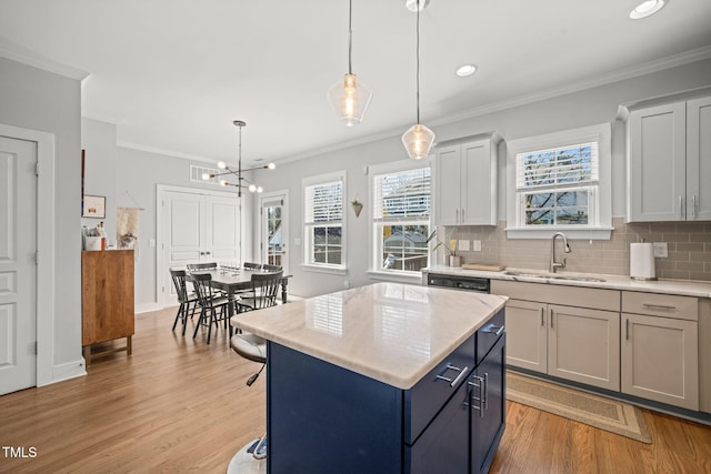 kitchen with a sink, a kitchen island, light countertops, hanging light fixtures, and decorative backsplash