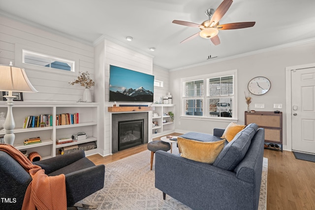 living area featuring crown molding, ceiling fan, a glass covered fireplace, and light wood-style floors