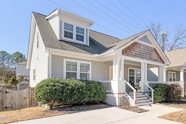 view of front of property with a porch, a shingled roof, and fence