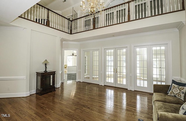 unfurnished living room with french doors, a chandelier, ornamental molding, dark hardwood / wood-style flooring, and a high ceiling